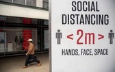 圖為英國倫敦一名男子從提示人們保持社交距離的牌子旁走過。（圖源：新華社）