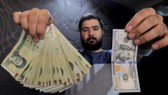 Một nhà đổi tiền ở thủ đô Tehran của Iran trưng tờ 100 USD (phải) và số tiền tương ứng bằng đồng Rial hôm 20-1-2016 - Ảnh: REUTERS