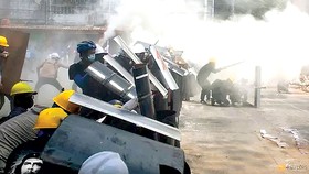 Người biểu tình ở Yangon che chắn đạn khói bằng các tấm khiên. Ảnh: REUTERS