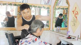 Anh Lê Minh Tân đang cắt tóc miễn phí cho một cụ già neo đơn