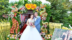 Cô dâu, chú rể chụp ảnh bên cổng cưới kết từ lá dừa, hoa, quả…