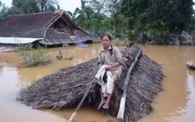 在一片汪洋的洪水之中，一名婦女坐在草屋頂上等待營救。（圖源：互聯網）
