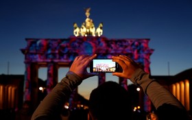 10月7日，在德國柏林，一名遊客拍攝被燈光點亮的勃蘭登堡門。（圖：新華社）