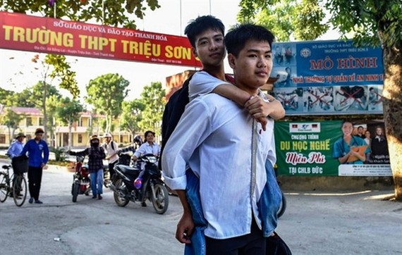 Ngo Minh Hieu carries his classmate Nguyen Tat Minh on his back to school every day. — Photo: nld.com.vn