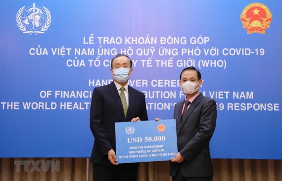 Thứ trưởng Bộ Ngoại giao Lê Hoài Trung trao tượng trưng số tiền 50.000 USD của Chính phủ và nhân dân Việt Nam đến Trưởng Đại diện Tổ chức Y tế Thế giới tại Việt Nam Kidong Park. Ảnh: TTXVN