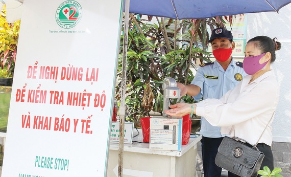 Nhân viên bảo vệ Trung tâm Y tế Thảo Điền, quận 2, TPHCM hướng dẫn người dân  sát khuẩn trước khi vào trung tâm. Ảnh: HOÀNG HÙNG