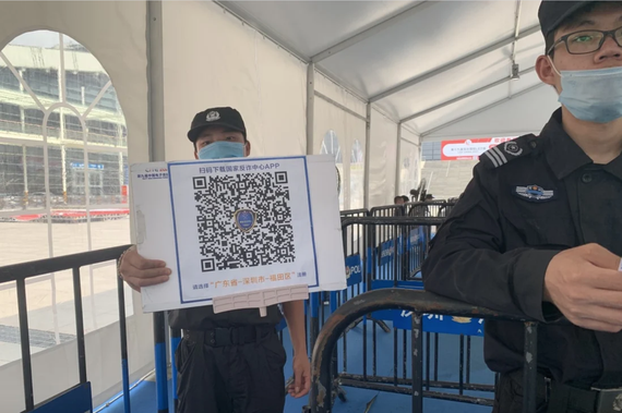 Nhân viên bảo vệ cầm tấm biển có mã QR để du khách quét và tải xuống ứng dụng tại lối vào của Trung tâm Triển lãm và Hội nghị Thâm Quyến vào 12-4-2021. Ảnh: Yujie Xue/SCMP