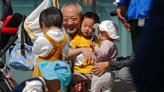 Một người đàn ông lớn tuổi chơi với trẻ em gần một tòa nhà văn phòng thương mại ở Bắc Kinh vào ngày 10 tháng 5 năm 2021. (AP)
