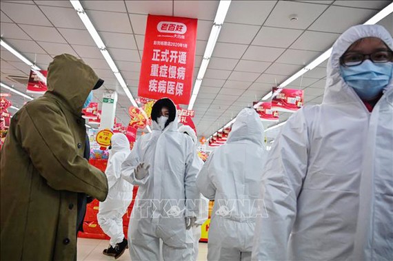 Nhân viên mặc quần áo bảo hộ và khẩu trang phòng chống dịch bệnh viêm phổi lạ do nhiễm virus corona phục vụ khách hàng tại một nhà thuốc ở Vũ Hán, Trung Quốc, ngày 25/1. Ảnh: AFP/TTXVN