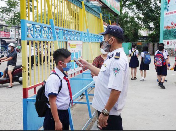 School security guard takes temperature of a student before he enters the school. (Photo: SGGP)