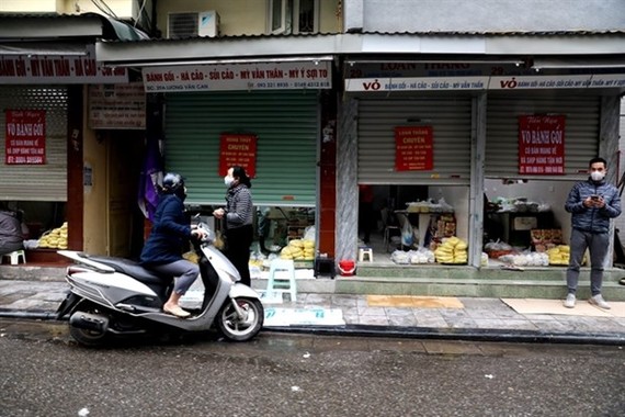 Stores on Hanoi's Luong Van Can Street half close their doors, only serve take-aways or online orders due to the impact of COVID-19 (Photo: VNA)
