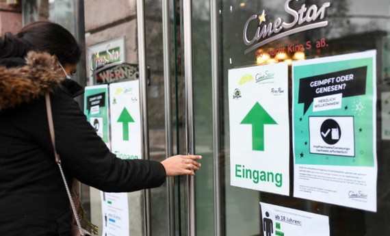 去年12月3日，在德國法蘭克福一家電影院外，一名女子從張貼防疫提示牌的入口處進入。（圖：新華社）