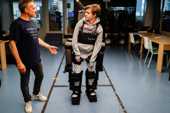Jean-Louis Constanz hướng dẫn cậu con trai Oscar 16 tuổi của mình sử dụng bộ khung xương trợ lực tại trụ sở Wandercraft, Paris, Pháp. Nguồn ảnh: Reuters.