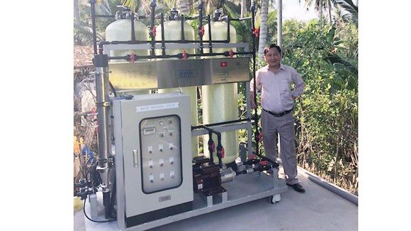GS Nguyễn Văn Phước và mô hình xử lý nước lắp đặt tại ấp An Quy. Ảnh: IER